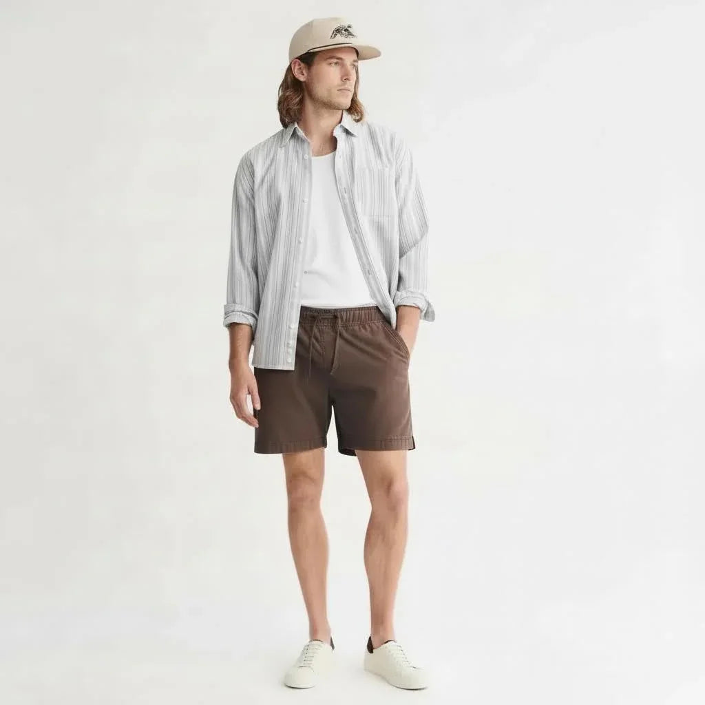 Man wearing brown shorts, white t-shirt, striped shirt, beige cap, and white sneakers