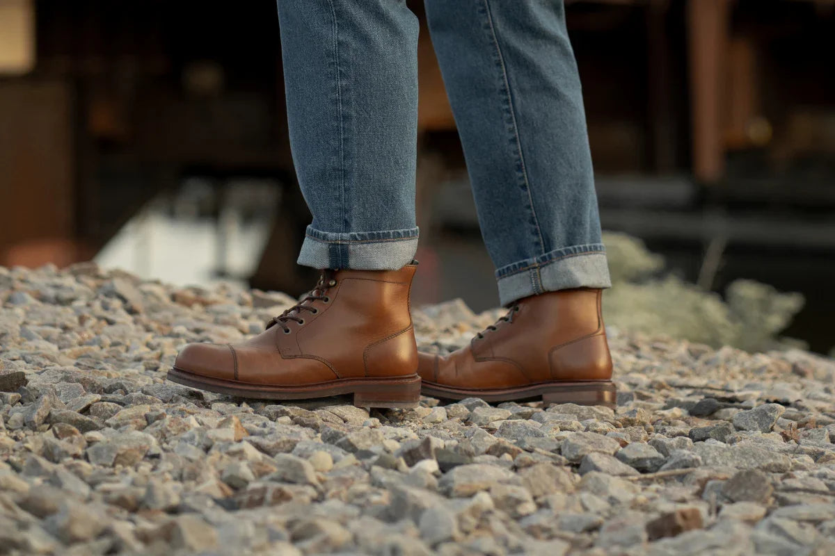 Brown leather lace-up boots with jeans on gravel outdoors