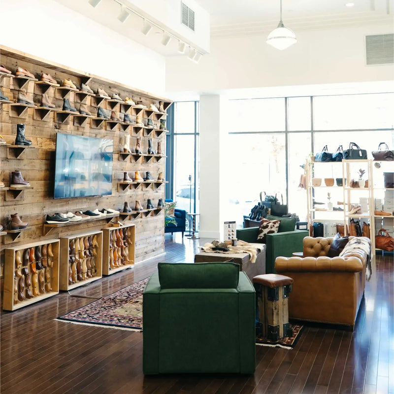 Modern shoe store interior with leather boots on wooden shelves, bags on display, and stylish seating area