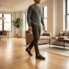 Man wearing dark loafers, olive pants, and gray sweater walking in modern living room