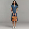 Woman in blue denim dress holding tan leather satchel handbag, fashion studio shot