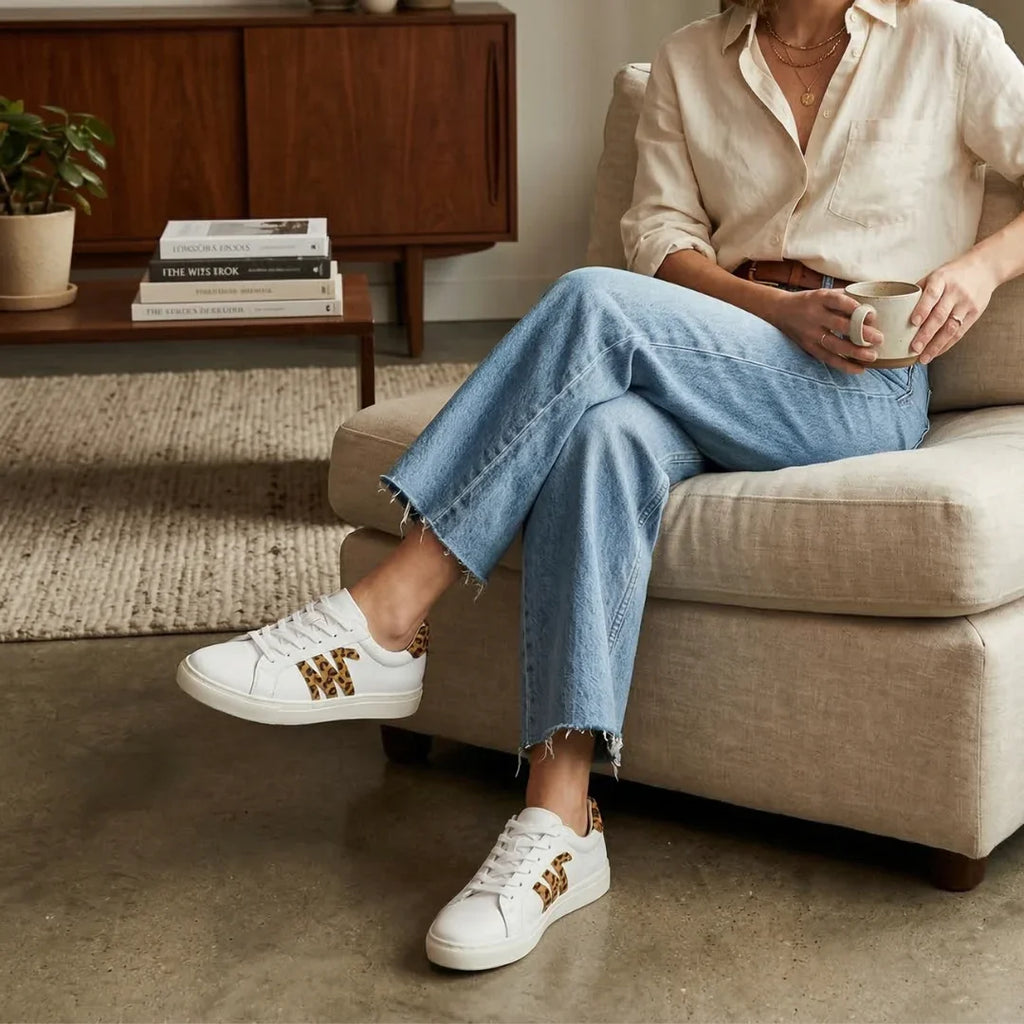 Woman wearing light jeans and leopard print white sneakers sitting on a beige sofa