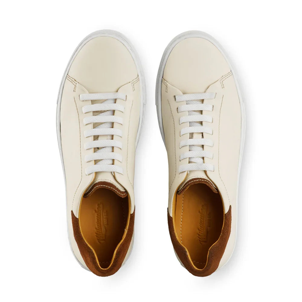 Top view of cream leather sneakers with brown suede heel accents and white laces on white background.