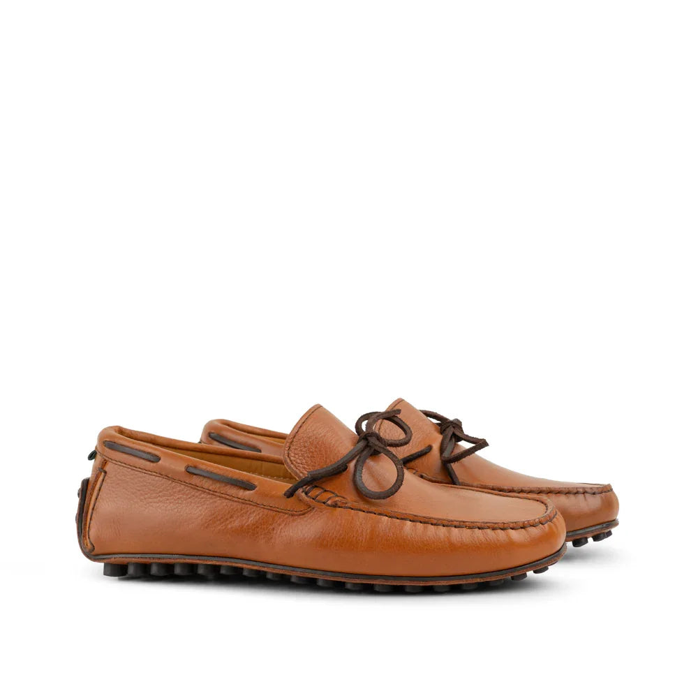 Pair of cognac brown leather driving loafers with rubber soles and lace detail on white background