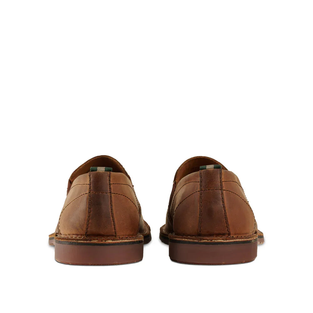 Rear view of camel brown leather slip-on shoes with stitched detailing on white background.